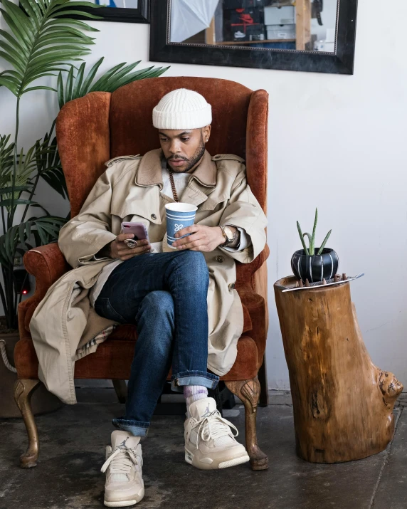 a man sitting in a chair reading a book, trending on unsplash, wearing a long coat, non binary model, iced latte, riyahd cassiem