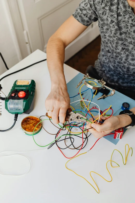 a woman sitting at a table working on a project, by Matthias Stom, trending on pexels, process art, revealing wires and electronics, holding controller, teaching, at home