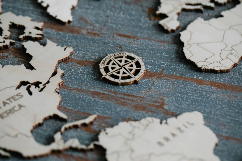 a map of the world with a compass on it, a jigsaw puzzle, by Daniel Lieske, trending on unsplash, conceptual art, made of intricate metal and wood, close up shot from the side, silver insignia, navy