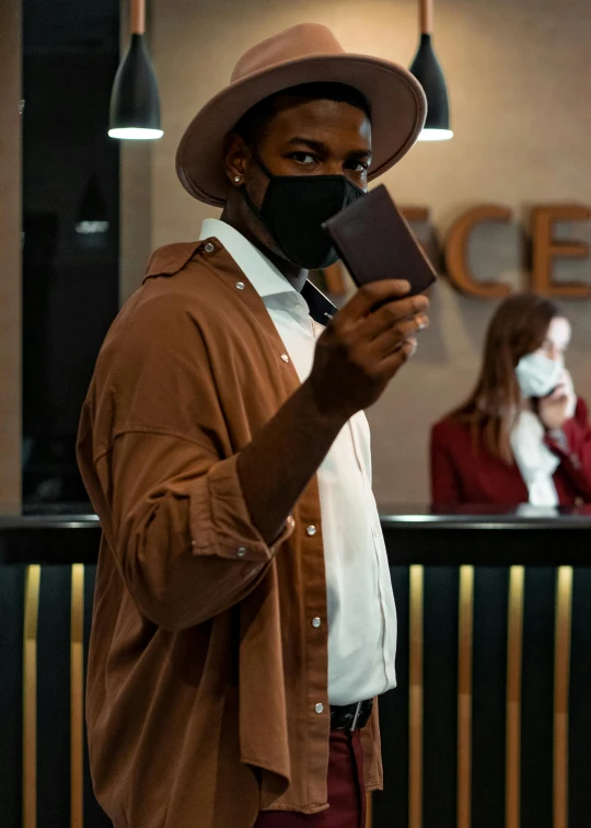a man wearing a face mask and holding a cell phone, pexels contest winner, renaissance, caracter with brown hat, tech robes, thumbnail, dark skinned