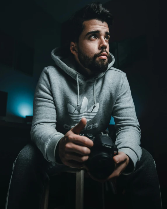 a man sitting on a stool holding a video game controller, inspired by Alejandro Obregón, pexels contest winner, drake's face, portrait soft low light, headshot profile picture, wearing adidas clothing