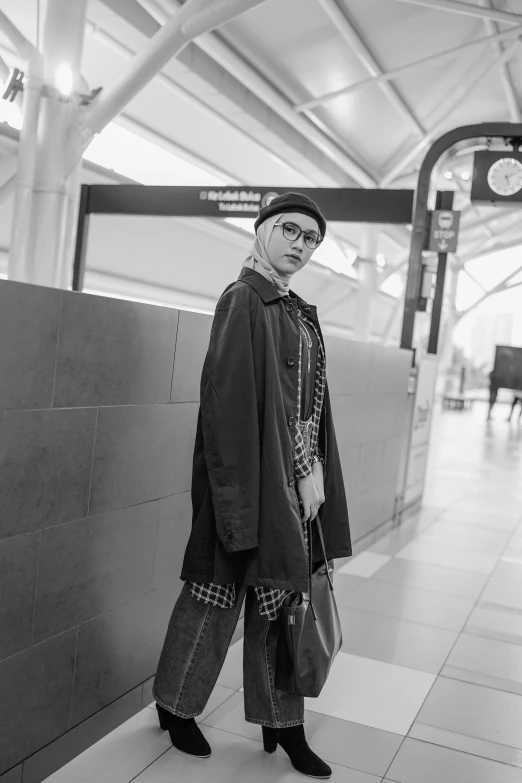 a black and white photo of a woman standing next to a wall, a black and white photo, unsplash, hyperrealism, in a subway, tartan cloak, in square-rimmed glasses, appearing in a shopping mall