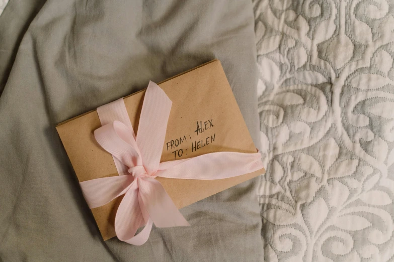 a brown box with a pink ribbon on top of a bed, by Alice Mason, pexels contest winner, letters, folded, satin, message