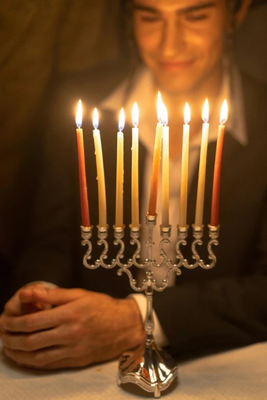 a man sitting at a table with a lit menorah, lights, to, getty images, jen atkin