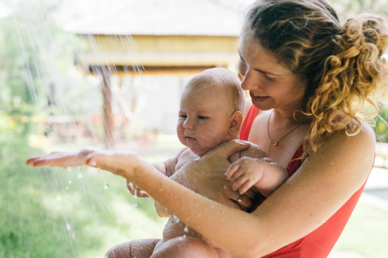 a woman holding a baby in the rain, by Elizabeth Durack, pexels contest winner, process art, having fun in the sun, bath, confident looking, thumbnail