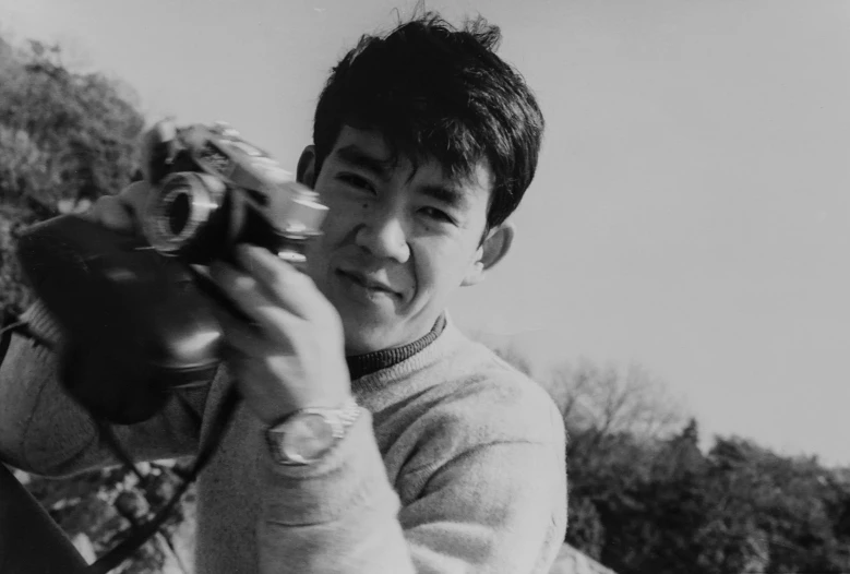 a black and white photo of a man holding a camera, a black and white photo, shin hanga, around 1 9 years old, qiu fang, lovingly looking at camera, close - up photograph