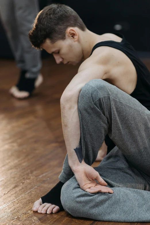 a man sitting on the floor in a dance studio, a tattoo, trending on pexels, hyperrealism, up to the elbow, low quality photo, thin young male, texture detail