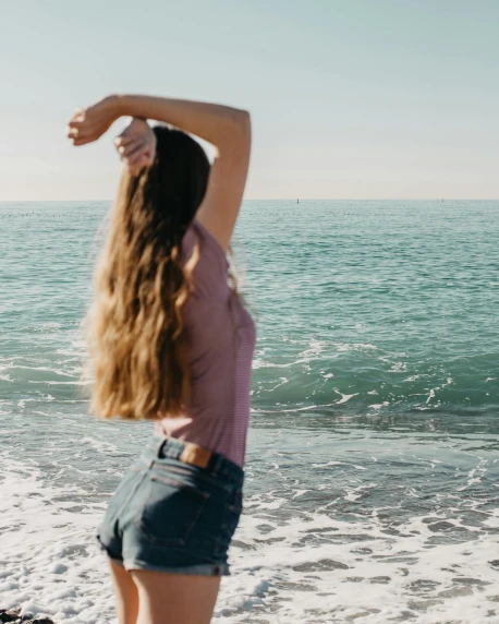a woman standing on top of a beach next to the ocean, wavy hair combed to one side, queer woman, arms out, photo of slim girl