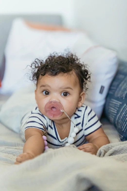 a baby laying on top of a bed next to a pillow, by Arabella Rankin, pexels contest winner, blowing bubblegum, mixed race, long hook nose, slightly open mouth