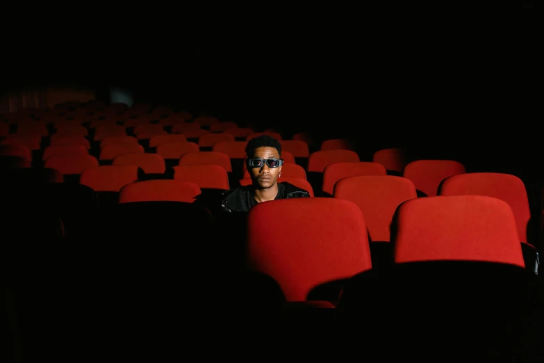 a man sitting in the middle of rows of red chairs, an album cover, pexels, realism, wearing 3 d glasses, gallant, out in the dark, in a cinema