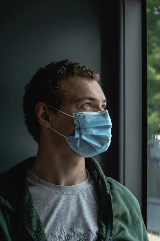 a man wearing a face mask looking out a window, a picture, 2 4 - year - old man, medium head to shoulder shot, dark. no text, surgery