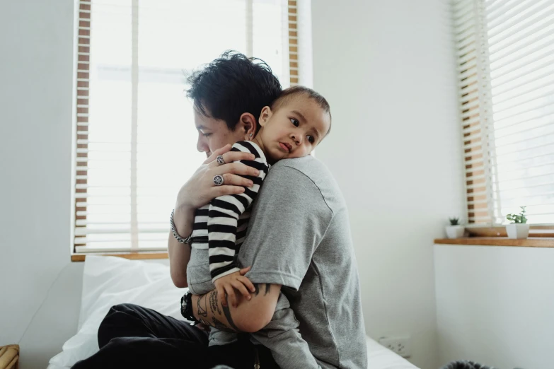 a man sitting on top of a bed holding a baby, pexels contest winner, hurufiyya, hugging each other, asian descent, boy with neutral face, bedhead