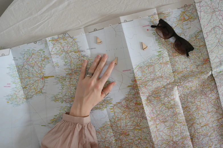 a person looking at a map with a pair of sunglasses on top of it, by Helen Stevenson, trending on pexels, rings, hands reaching for her, white and pink cloth, northern france