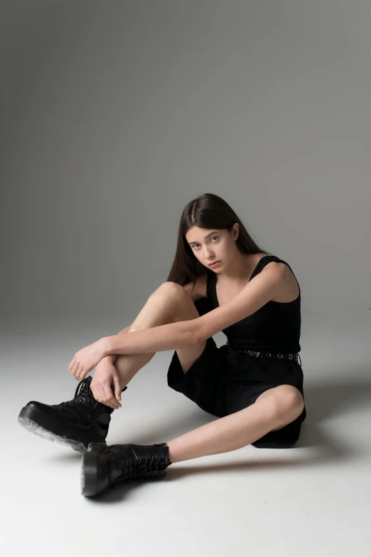 a woman in a black dress is sitting on the floor, trending on pexels, wearing tall combat boots, non binary model, she is about 1 6 years old, jen atkin