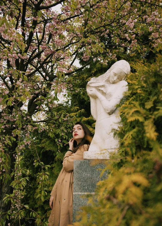 a woman standing next to a statue in a park, unsplash, romanticism, blossoming, ✨🕌🌙