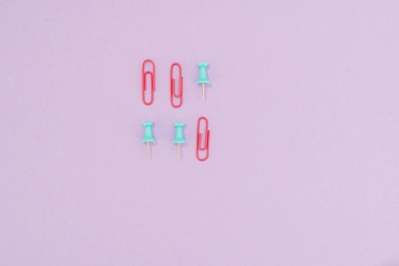 a couple of paper clips sitting on top of a pink surface, by Emma Andijewska, trending on pexels, minimalism, red and cyan, bullets, miniatures, green and purple color scheme