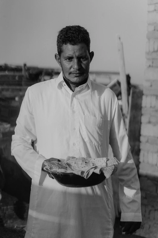 a black and white photo of a man holding a plate of food, by Maurycy Gottlieb, arabia, 8 k image