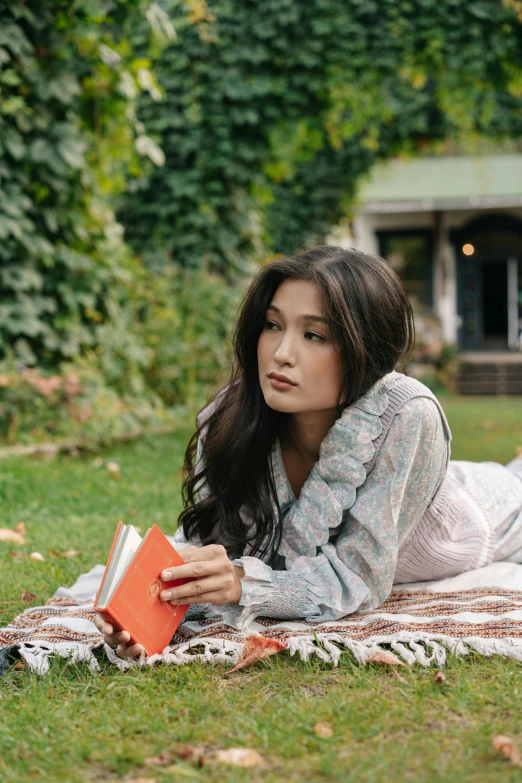 a woman laying on a blanket reading a book, gemma chan, in the garden, thoughtful ), holding notebook