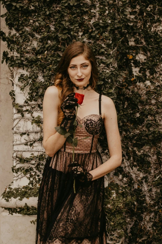 a woman standing in front of a wall holding a rose, an album cover, inspired by Elsa Bleda, renaissance, wearing a gothic dress, katherine mcnamara inspired, southern gothic art, pose 4 of 1 6