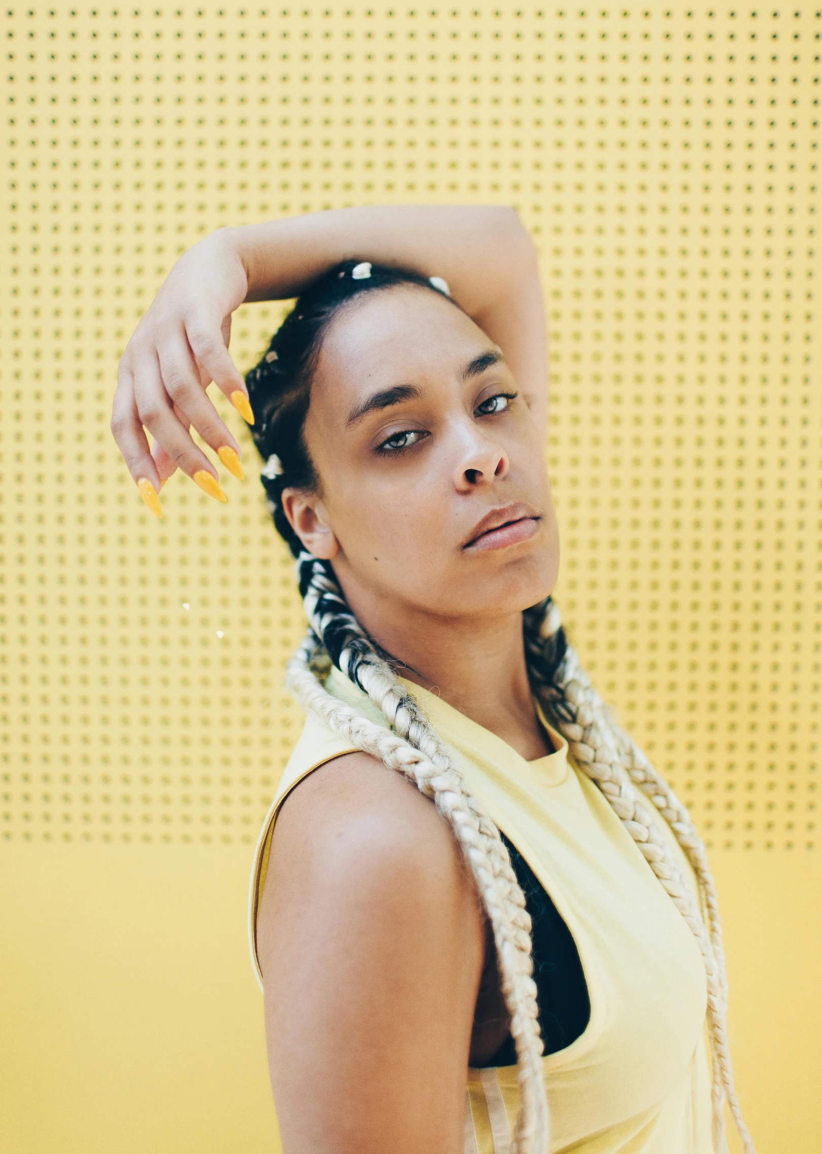 a woman standing in front of a yellow wall, an album cover, long cornrows, looking towards camera, mixed-race woman, profile image