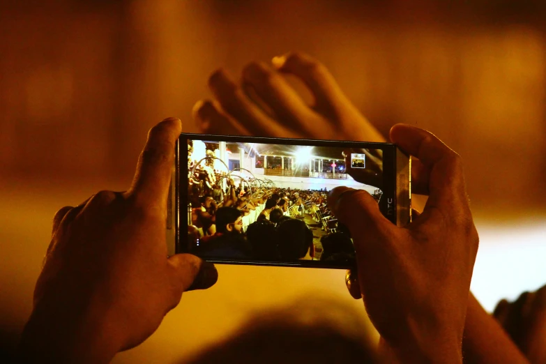 a person holding up a cell phone to take a picture, happening, 2 0 1 5 live music video, lit from above, slide show, night time footage