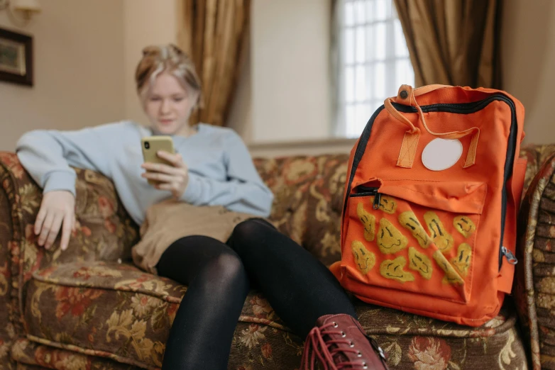 a woman sitting on a couch looking at her cell phone, inspired by Sarah Lucas, trending on pexels, graffiti, wearing strawberry backpack, coloured in orange fire, in a classroom, sophie turner