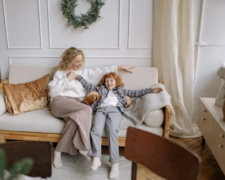 a woman sitting on top of a couch next to a child, pexels contest winner, brown clothes, curly blond, plush furnishings, wearing elegant casual clothes