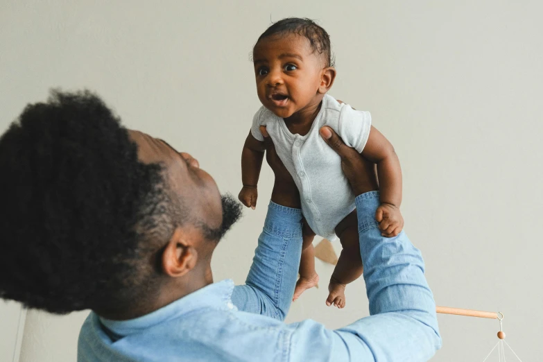 a man holding a baby up in the air, by Carey Morris, pexels contest winner, brown skin, looking cute, healthcare, rectangle