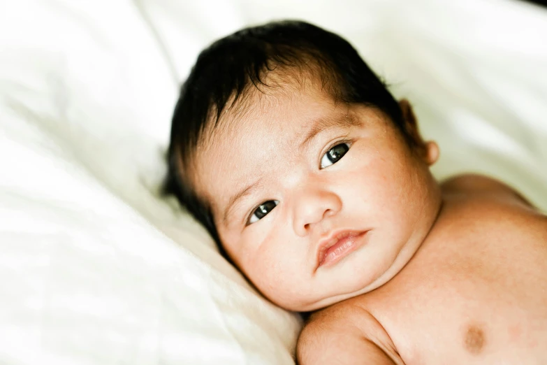 a close up of a baby laying on a bed, by Gavin Hamilton, shutterstock contest winner, hurufiyya, mixed race, portrait image, david nakayama, the birth