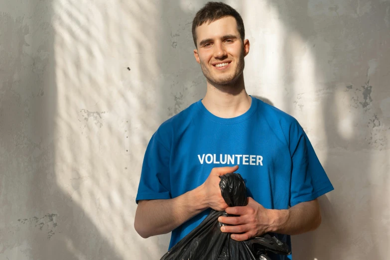 a man in a blue shirt holding a black bag, pexels contest winner, plasticien, wearing a t-shirt, avatar image, rubbish, promotional image