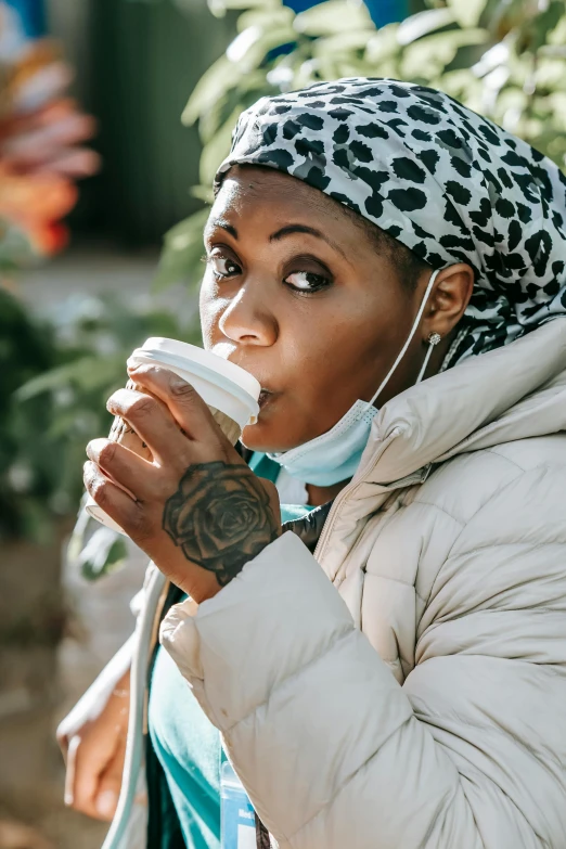 a woman drinking a cup of coffee while wearing a face mask, trending on pexels, happening, in a hood, qiyana, chewing, iced latte