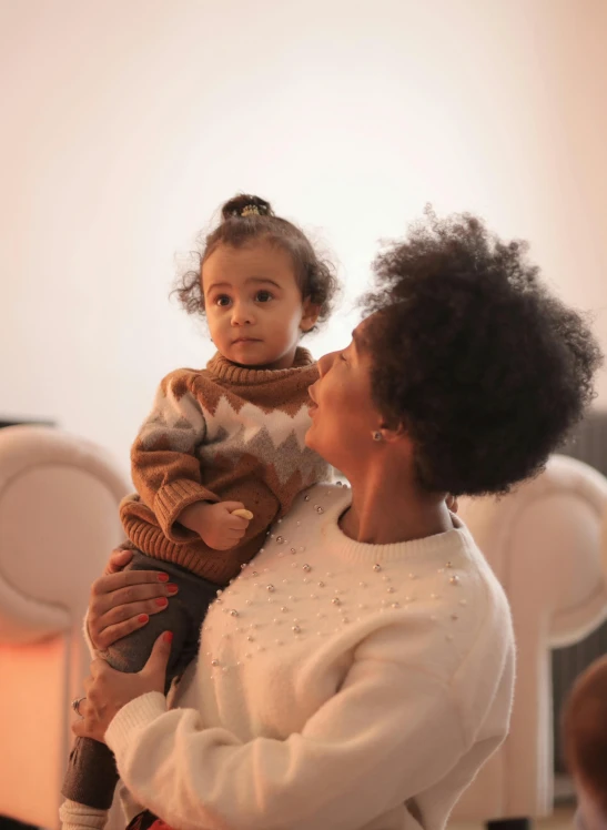 a woman holding a small child in her arms, by Adam Saks, pexels, with afro, square, sitting down, warm coloured