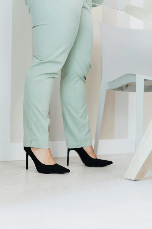 a woman in high heels standing next to a chair, by Nina Hamnett, trending on pexels, green corduroy pants, grey pants and black dress shoes, pastel green, detailed product shot