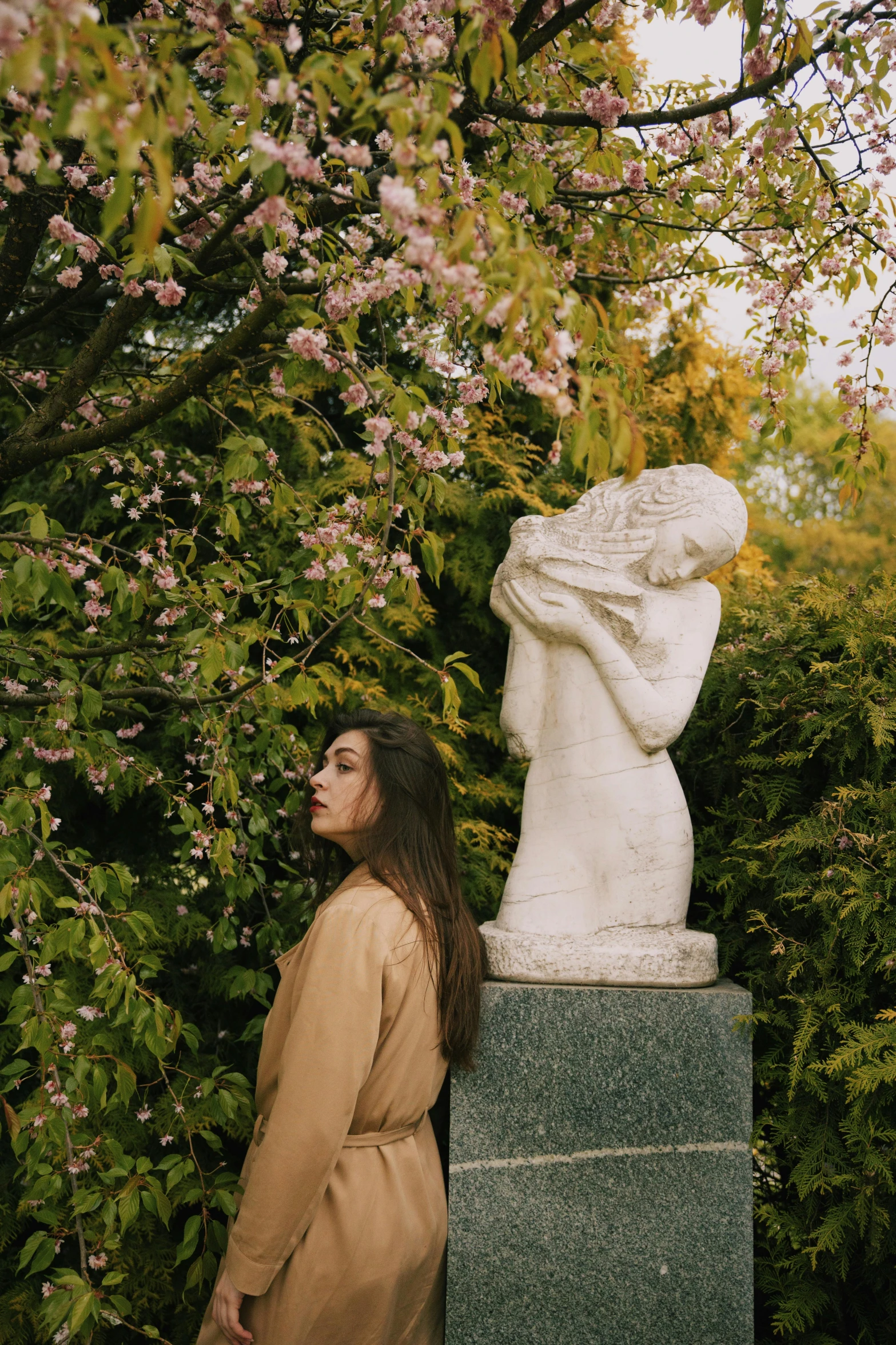 a woman standing next to a statue in a park, inspired by Elsa Bleda, unsplash, art nouveau, blossoming, still from a music video, in a garden of a house, thoughtful )