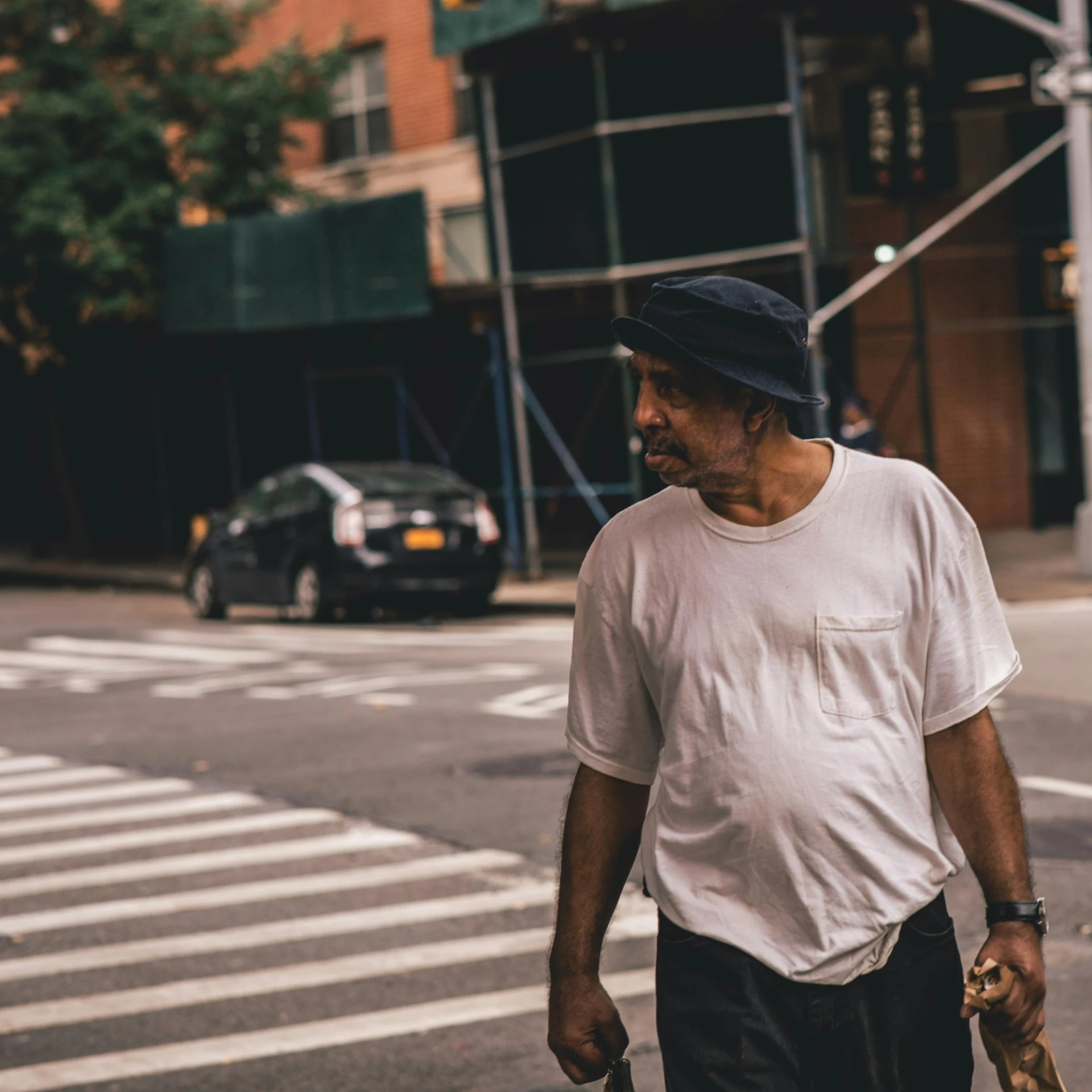 a man walking across a street holding a skateboard, a photo, blind brown man, new york streets, portrait featured on unsplash, elderly