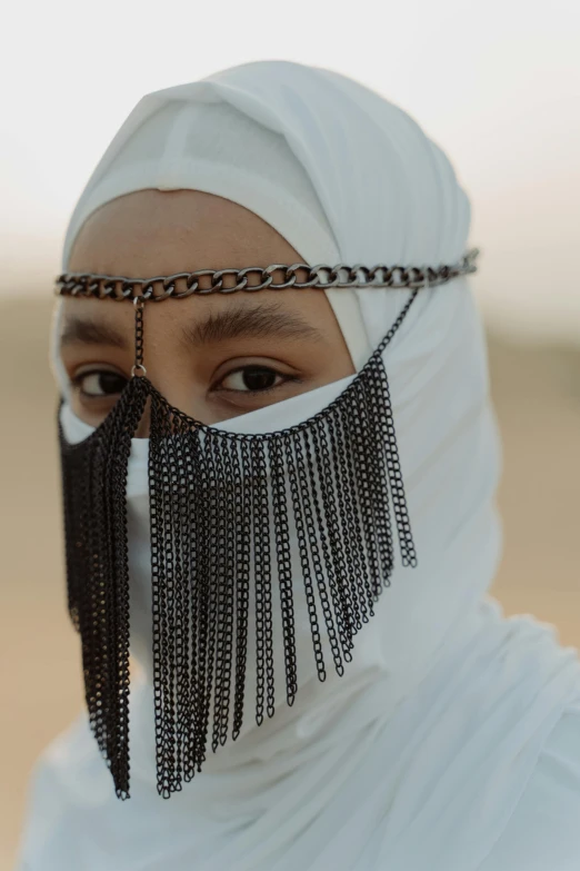 a close up of a person wearing a face mask, inspired by Yehia Dessouki, trending on unsplash, afrofuturism, desert robe, wearing chains, white hijab, still from film