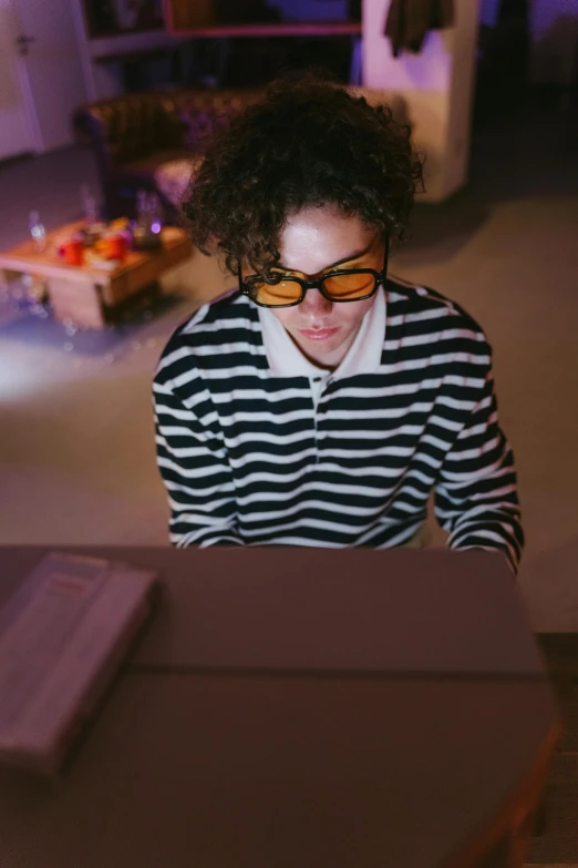 a woman sitting at a table in front of a laptop computer, an album cover, by Jacob Toorenvliet, trending on pexels, computer art, wearing orange sunglasses, stripes, flashing lights, androgynous person