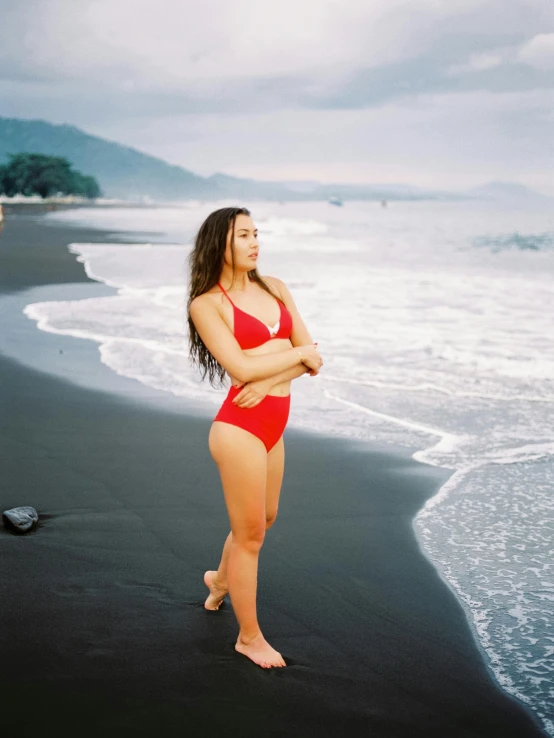 a woman standing on a beach next to the ocean, red body suit, portrait of modern darna, profile image, wavy