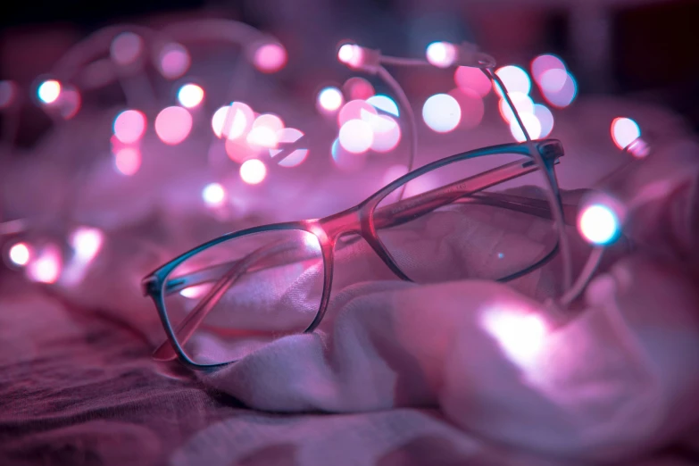 a pair of glasses sitting on top of a bed, by Adam Marczyński, trending on pexels, aestheticism, fairy lights, blue and pink, in square-rimmed glasses, enlightening