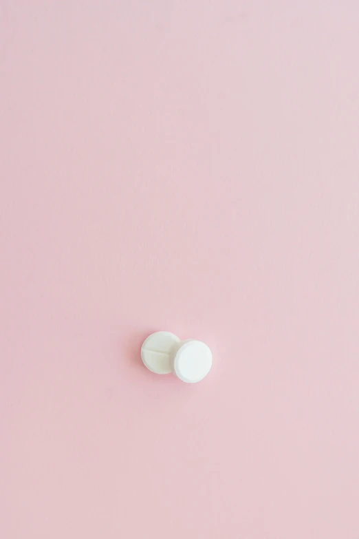 two white pills sitting on top of a pink surface, by Harvey Quaytman, jovana rikalo, buttons, milky white skin, flat minimalistic