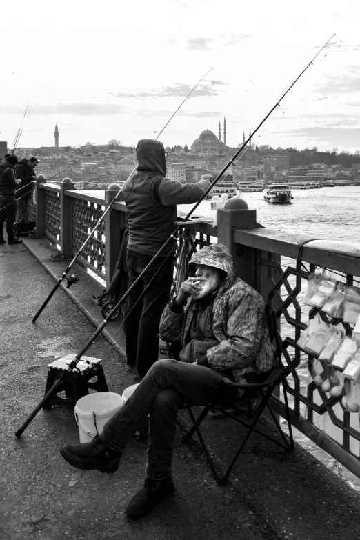 a man sitting on a bench next to a river, a black and white photo, by Nabil Kanso, fishing pole, fallout style istanbul, 2 5 6 x 2 5 6, on a bridge