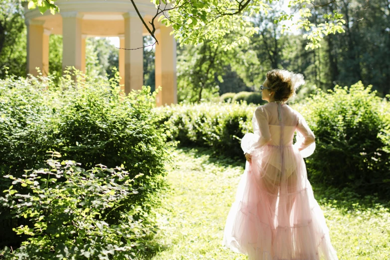 a woman in a pink dress standing in a garden, inspired by Konstantin Somov, tumblr, shot from the back, sheer fabrics, regency-era, on a bright day