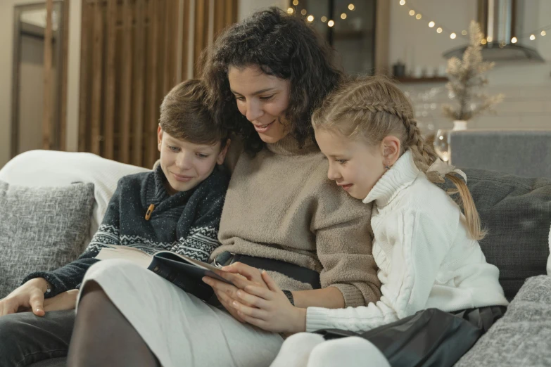 a woman and two children sitting on a couch reading a book, a cartoon, pexels, incoherents, kramskoi 4 k, technology, hygge, a handsome