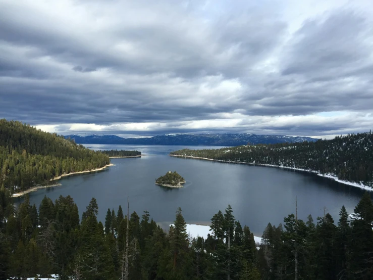 a large body of water surrounded by trees, by Whitney Sherman, unsplash, hurufiyya, big bear lake california, only snow in the background, an island floating in the air, grey cloudy skies