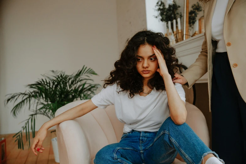 a woman sitting on top of a couch next to a man, by Emma Andijewska, trending on pexels, renaissance, brown curly hair, young angry woman, wearing jeans, sitting on a chair