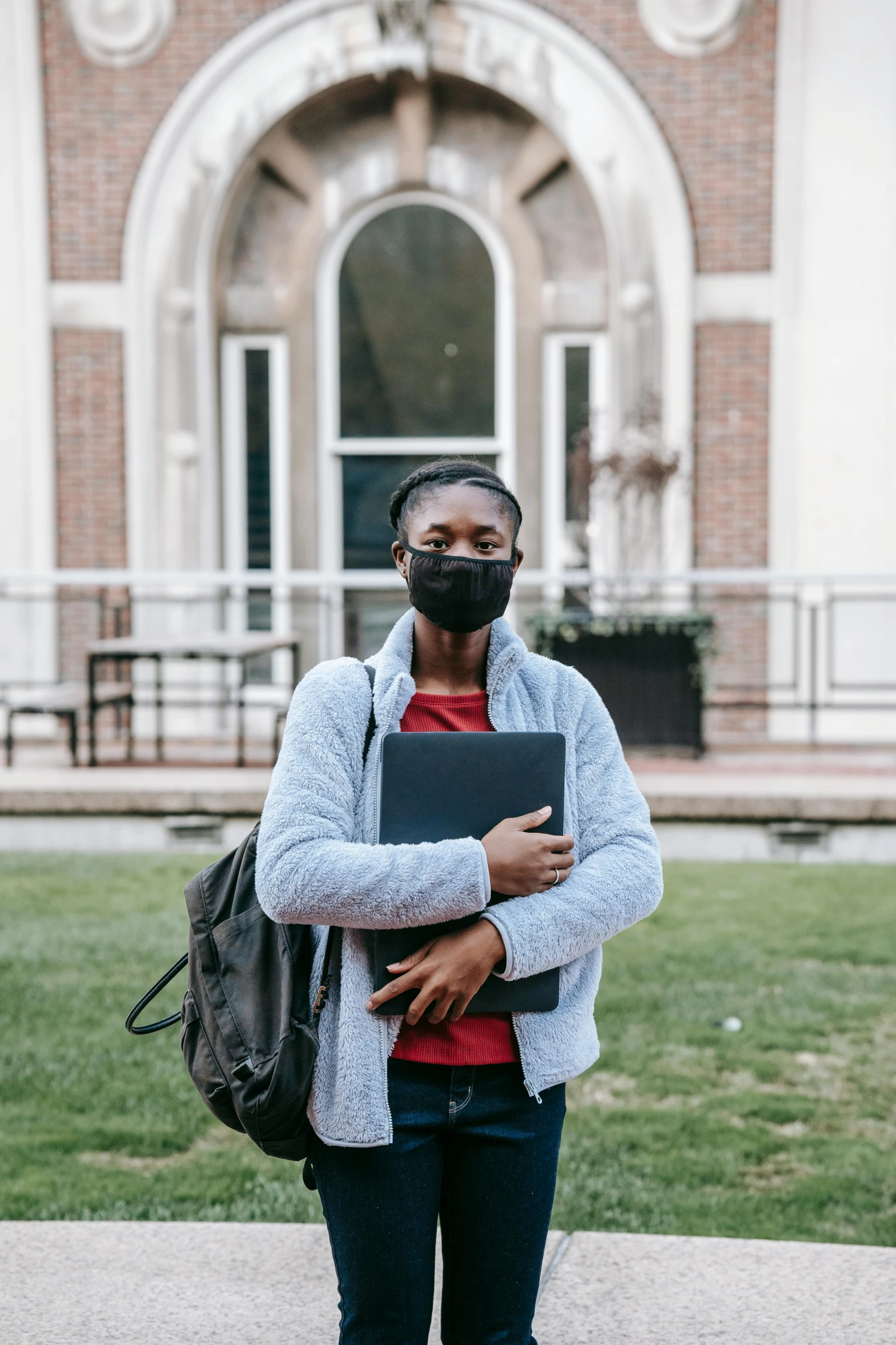 a man standing in front of a building with a laptop, mask off, black young woman, academic clothing, lgbtq