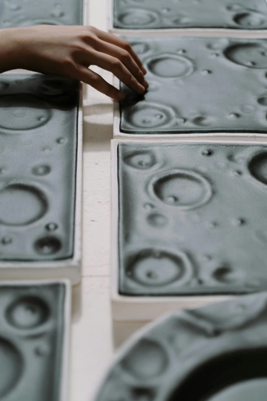 a close up of a person's hand on a tile, inspired by Vija Celmins, process art, moon craters, inside a space station, big production, plates