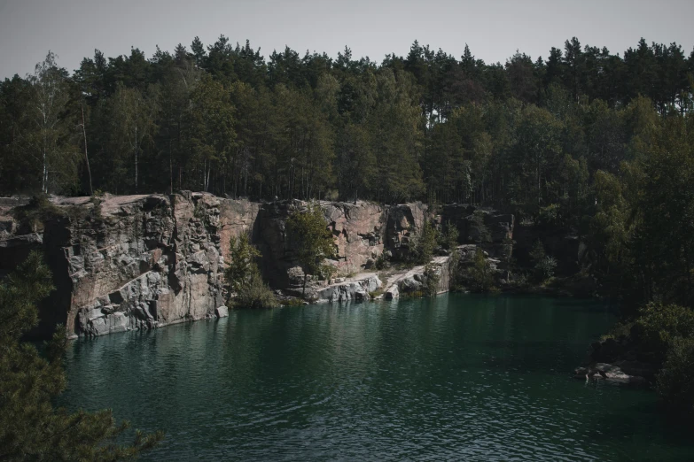 a large body of water surrounded by trees, inspired by Elsa Bleda, pexels contest winner, hurufiyya, rock quarry location, muspelheim, grey, [ cinematic