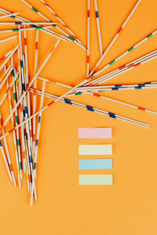 a bunch of pencils sitting on top of an orange surface, an album cover, by Nicolette Macnamara, unsplash, conceptual art, colorful striped pavillions, chopsticks, reeds, game