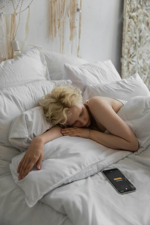 a woman laying on top of a bed next to a window, pexels contest winner, pale skin curly blond hair, gif, tired half closed, goddess checking her phone